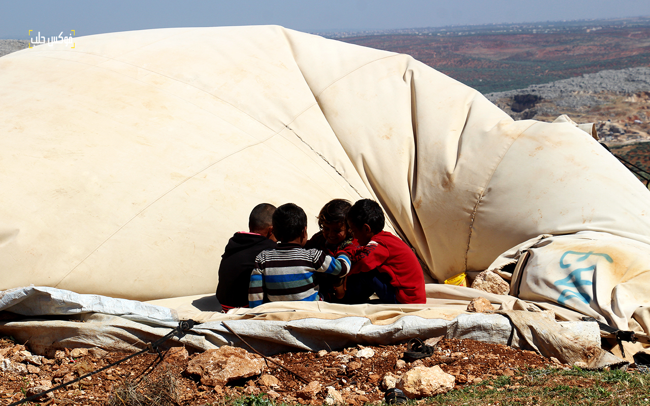 أطفال يجلسون على خيمتهم بعد أن هدمتها العاصفة الهوائية في مخيم كفتين بريف إدلب