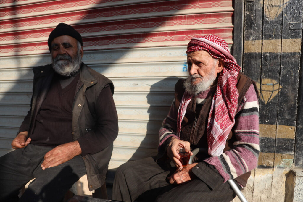 شخصان من كبار السن يشربان الشاي على أحد الأرصفة في مدينة كفرتخاريم . 10 كانون الأول 2024- رهام علي