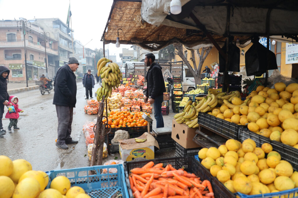 بائع فواكه جوال يعرض بضائعه على الشارع الرئيسي لمدينة كفرتخاريم غربي إدلب، شباط 2025- تصوير: رهام علي.
 

