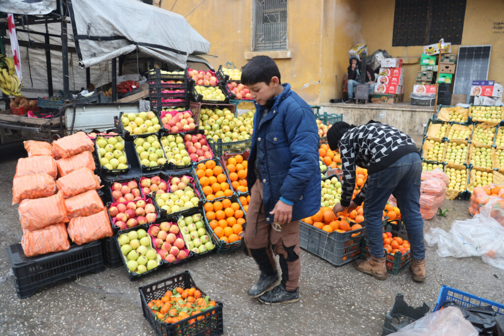 طفلان يعملان ببيع الفواكه على الطريق الرئيسي لمدينة كفرتخاريم غربي إدلب، شباط 2025- تصوير: رهام علي.