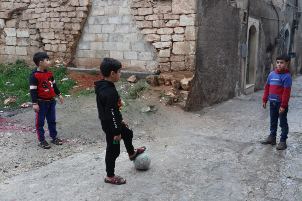 أطفال يلعبون بالكرة في أحد أزقة مدينة كفرتخاريم الضيقة، غربي إدلب، شباط 2025- تصوير: رهام علي.