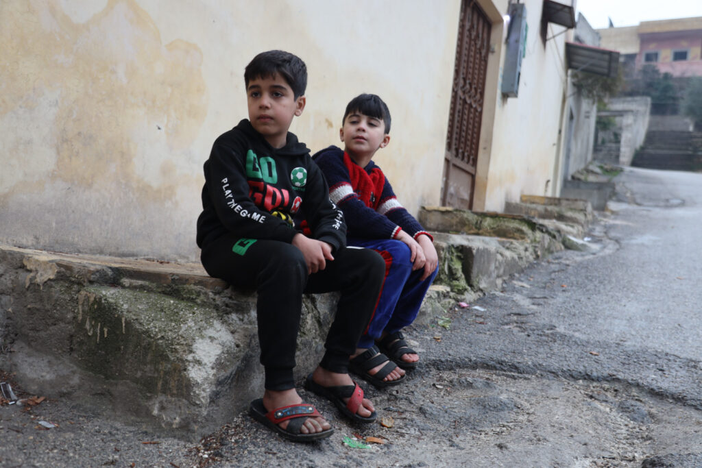 أطفال يجلسون على حافة طريق في مدينة كفرتخاريم غربي إدلب، شباط 2025- تصوير: رهام علي.
