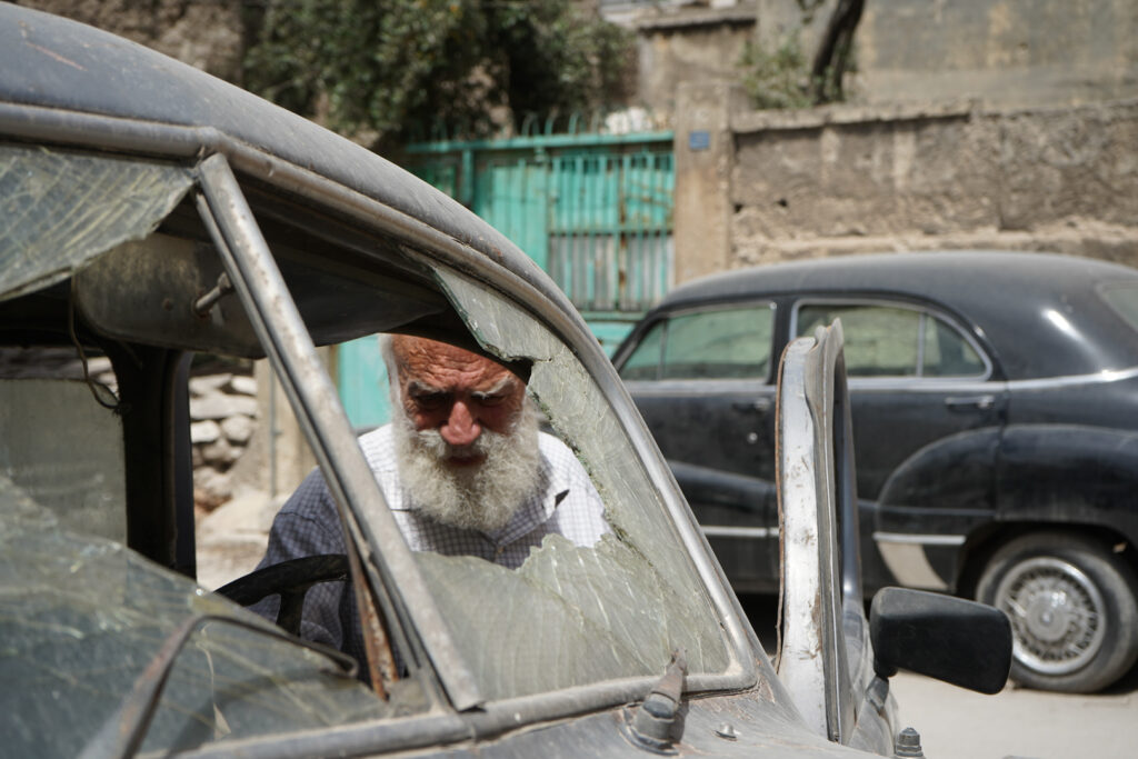 أبو عمر يتفقد سيارة والده موديل عام ، حي الشعار في مدينة حلب، 2025- تصوير: سحر زعتور.