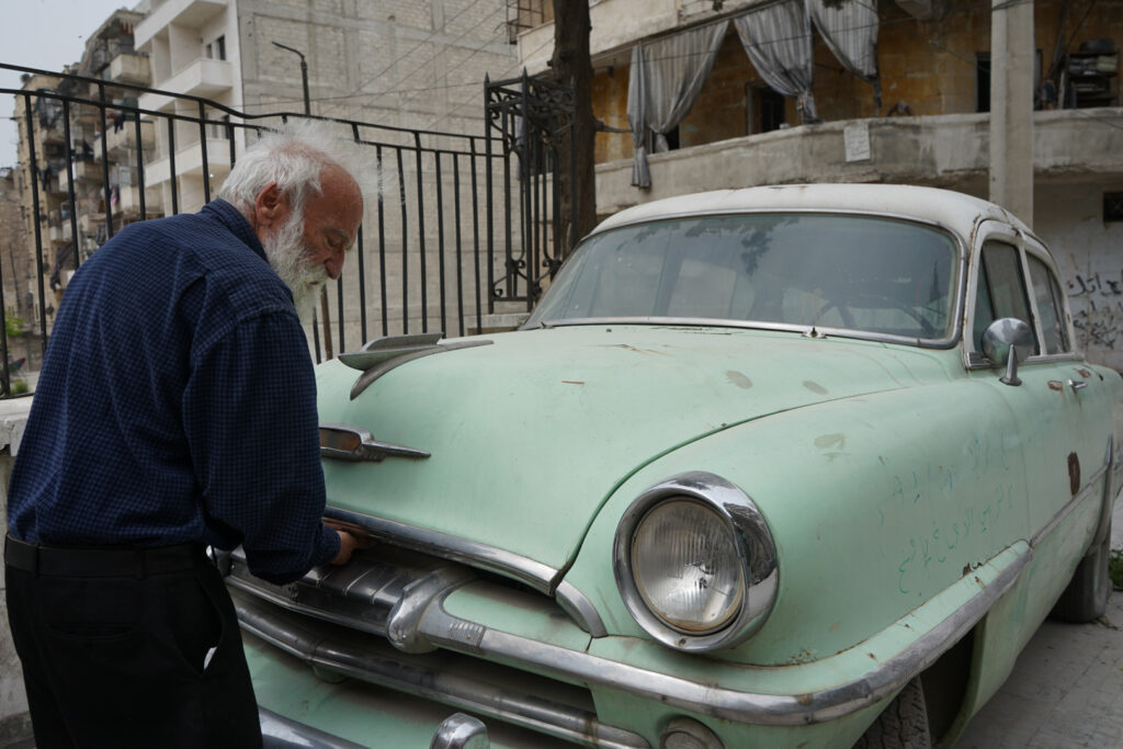 أبو عمر يعاين سيارته المركونة أمام منزله من طراز "بليموث" موديل أوائل الخمسينيات، حي الشعار في مدينة حلب، 2025- تصوير: سحر زعتور.