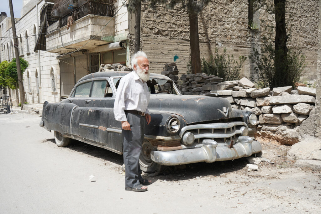 ابو عمر يقف أمام سيارة الكاديلاك المركونة أمام منزله، حي الشعار في مدينة حلب، 2025- تصوير: سحر زعتور.