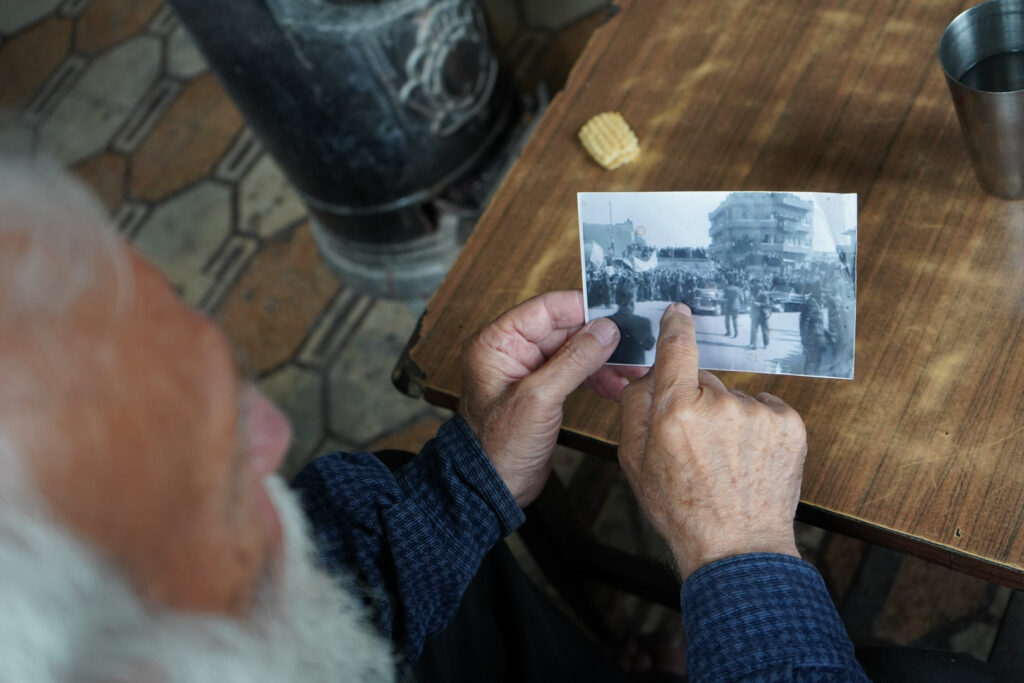 أبو عمر يتأمل صورة توثق لحظة استقبال الرئيس جمال عبد الناصر عام 1958 في ساحة سعدالله الجابري، حي الشعار في مدينة حلب، 2025- تصوير: سحر زعتور.