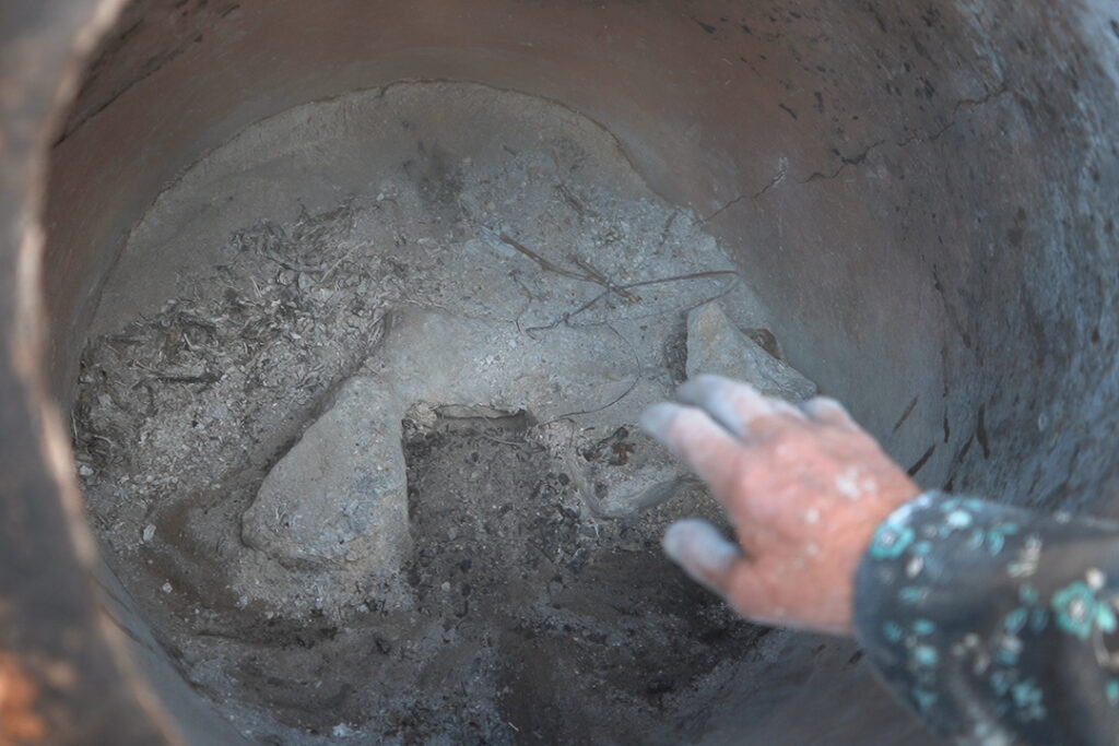 أم محمد تنظف التنور قبل إشعال النار استعدادًا للخَبز، كفرنبل، ريف إدلب، أيار 2025- تصوير: سحر زعتور
