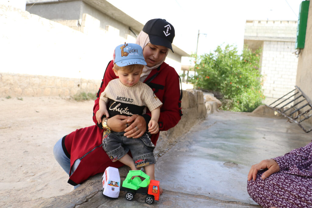 حلوم تلاعب أخاها جمعة أمام منزلهم بعد عودتها من العمل.  قرية مشمشان، جسر الشغور، أيار 2025- تصوير: هيام الباشا 