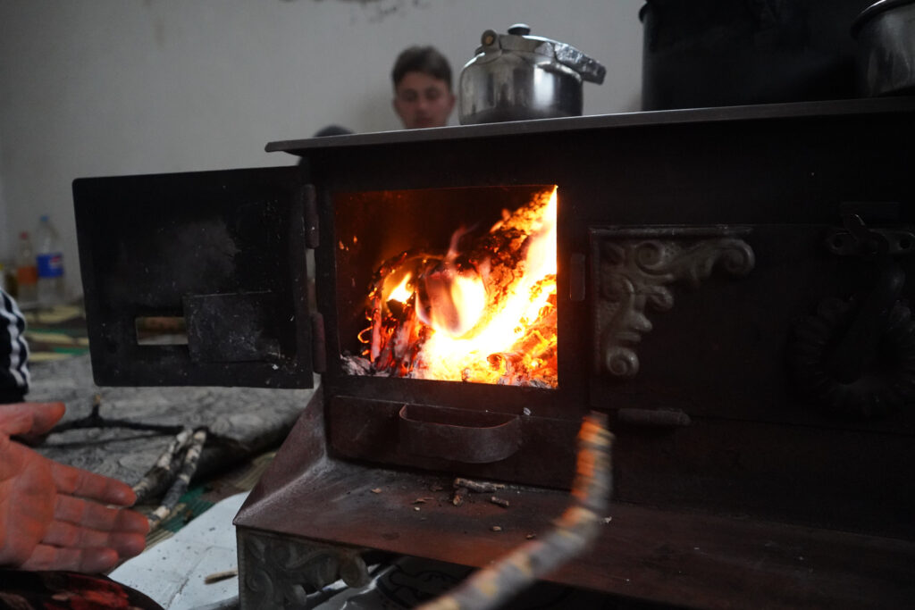 أم محمد تطهو الطعام وتعدّ الشاي على مدفأة الحطب لتوفير الغاز، كفرنبل، ريف إدلب، أيار 2025- تصوير: سحر زعتور
