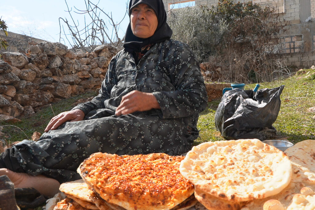 استراحة قصيرة بعد انتهاء أم محمد من الخَبز على التنور لعدم توفر الخُبز الطازج، كفرنبل، ريف إدلب، أيار 2025- تصوير: سحر زعتور