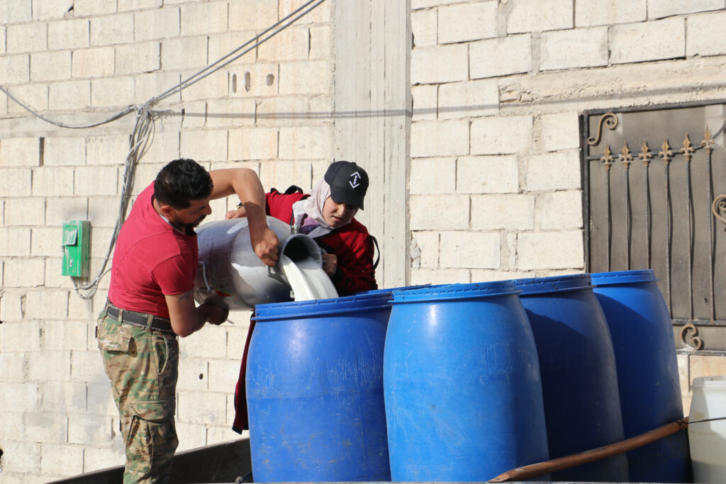 حلوم ووالدها يتعاونان على صب الحليب في البراميل. قرية مشمشان، جسر الشغور، أيار 2025- تصوير: هيام الباشا
