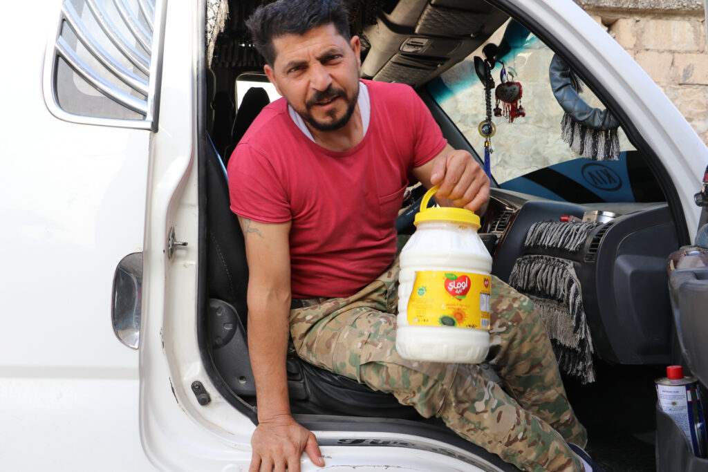 أبو جمعه والد حلوم يمسك في يده حليب جلبه لعائلته. قرية مشمشان، جسر الشغور، أيار 2025- تصوير: هيام الباشا
