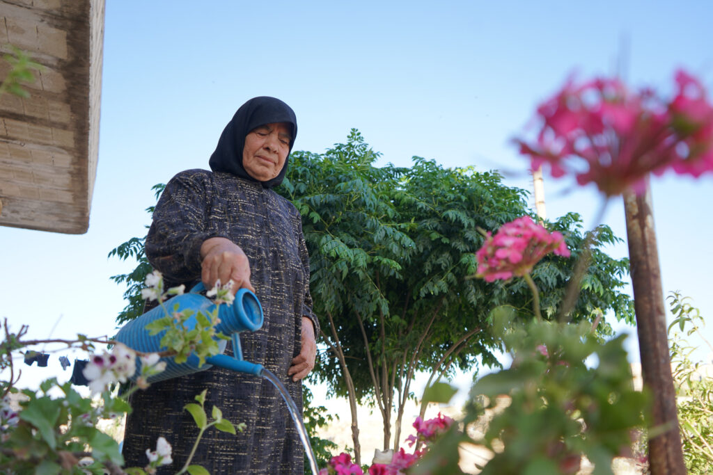 أم محمد تسقي الورود والأزهار التي زرعتها بعد عودتها، كفرنبل، ريف إدلب، أيار 2025- تصوير: سحر زعتو