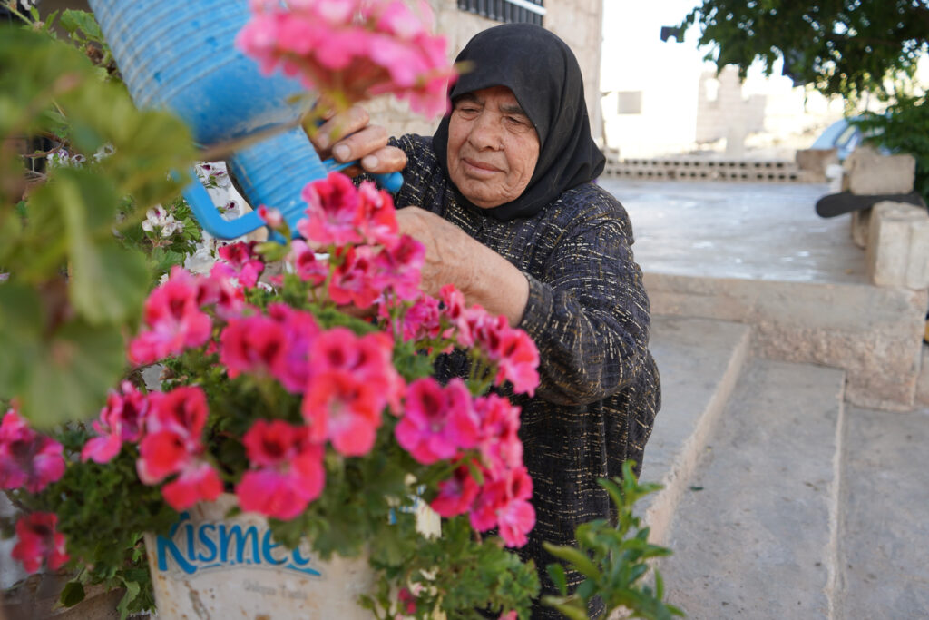  أم محمد تهتم بالورود والأزهار التي زرعتها بعد عودتها من المخيمات، كفرنبل، ريف إدلب، أيار 2025- تصوير: سحر زعتور