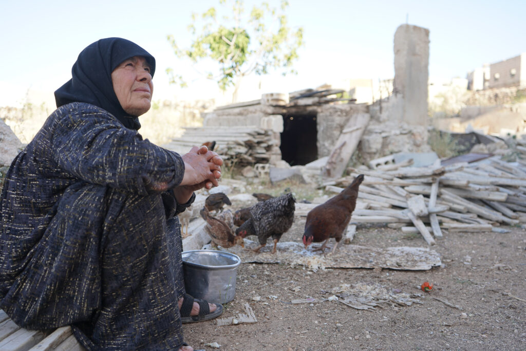 أم محمد تطعم الدجاجات أثناء غياب أبو محمد عن المنزل بسبب العمل، كفرنبل، ريف إدلب، أيار 2025- تصوير: سحر زعتور
