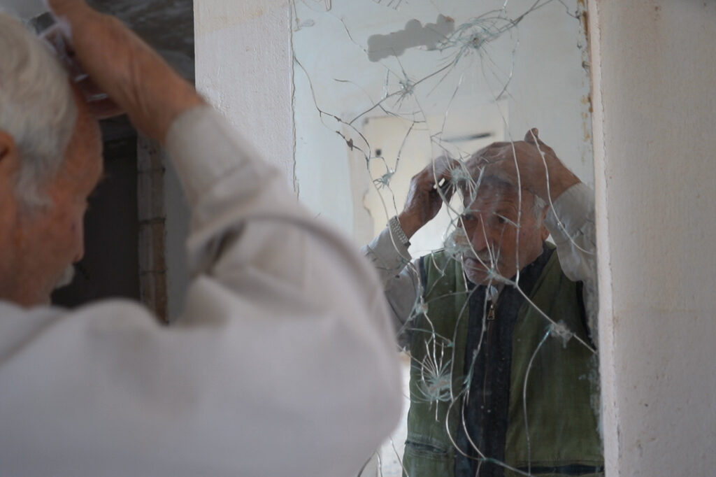 أبو محمد يمشط شعره أمام المرآة المكسورة، كفرنبل، ريف إدلب، أيار 2025- تصوير: سحر زعتور