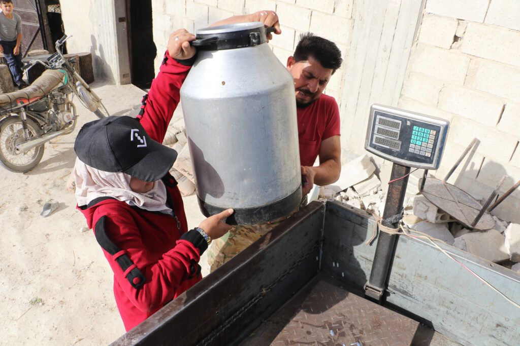 حلوم ووالدها يتعاونان على حمل جرة الحليب والتي تسع من 45 إلى 50 كغ. قرية مشمشان، جسر الشغور، أيار 2025- تصوير: هيام الباشا 
