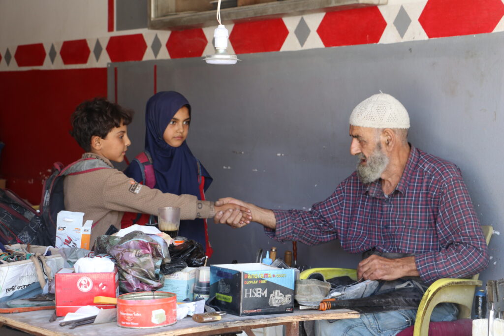 أبو محمود يستقبل حفيديه بعد عودتهما من المدرسة. خربة الجوز، ريف جسر الشغور. تشرين الأول 2025. تصوير: هيام الباشا