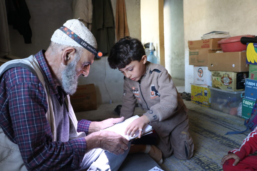 أبومحمود يتابع دراسة حفيديه. خربة الجوز، ريف جسر الشغور، تشرين الأول 2025. تصوير: هيام الباشا